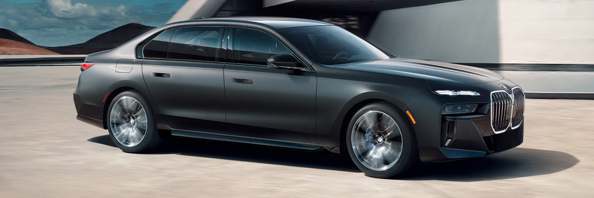 Side view of the 2023 BMW 7 Series parked on a concrete floor with mountains in the back