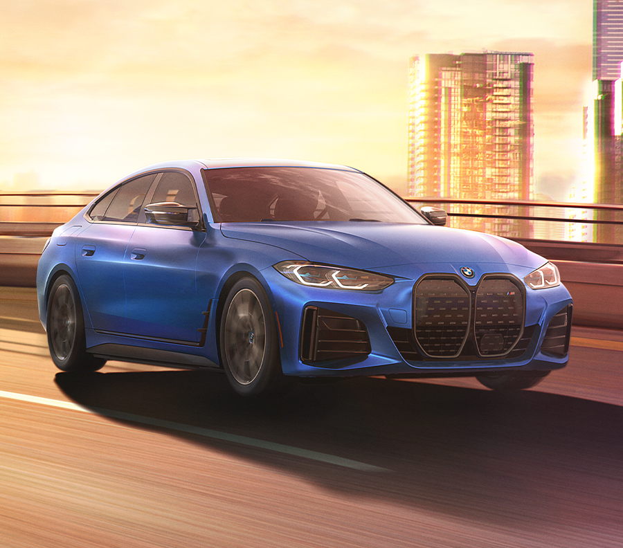 Exterior shot of a 2023 BMW i4 driving down a street with sunset in the background.