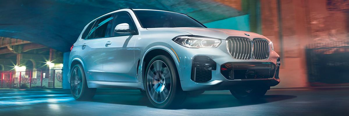 Side view of a 2023 BMW X5 accelerating through narrow city streets.