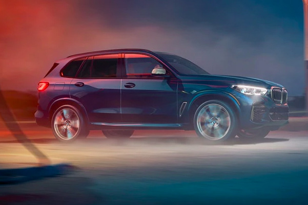 Side profile of 2023 BMW X5 M50i accelerating on road at night.