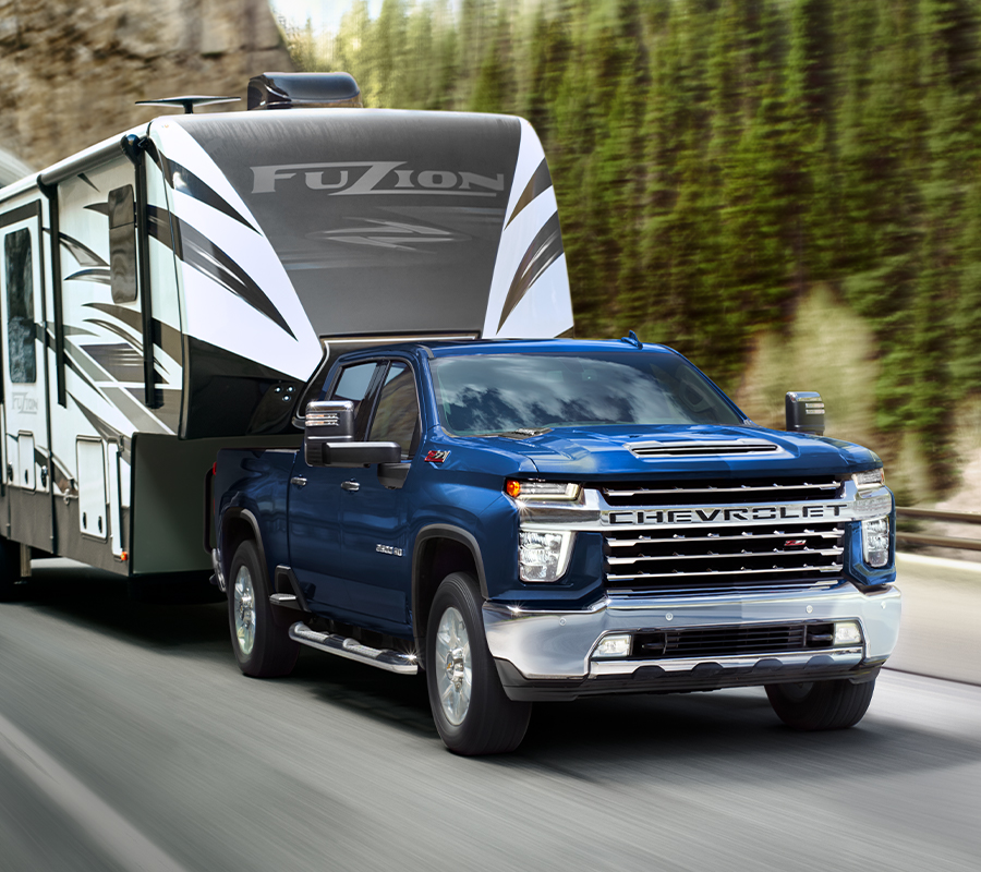 Blue 2023 Chevrolet Silverado HD towing RV trailer on road during day.