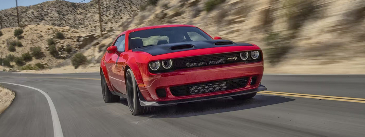 A red 2023 Dodge Challenger SRT Jailbreak being driven on a curved highway.