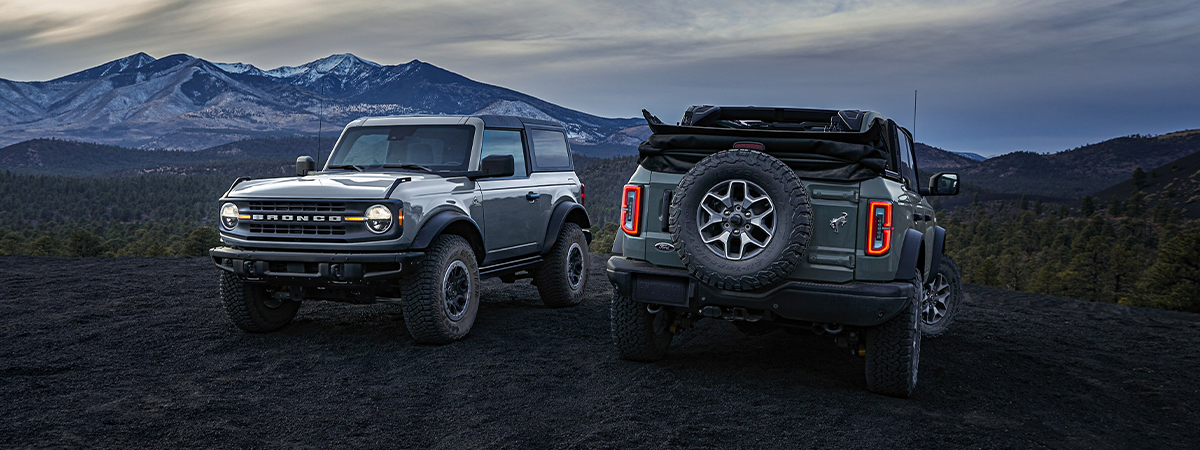Exterior shot of two 2023 Ford Broncos parked on a field with mountains in the background.