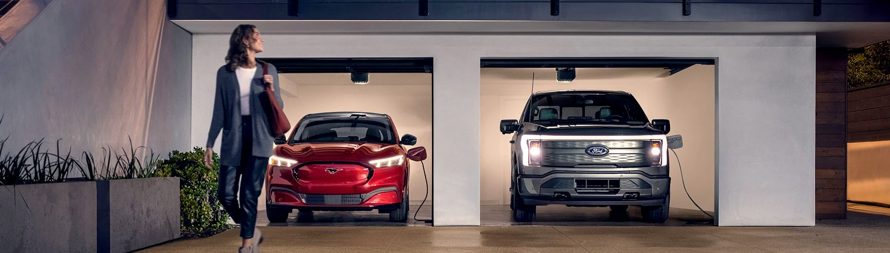 A 2022 Ford Mustang Mach-E® and a Ford F-150® Lightning are being charged in a garage at night near two people