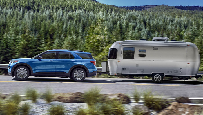 2023 Ford Explorer® Hybrid SUV towing a camper on a forest road
