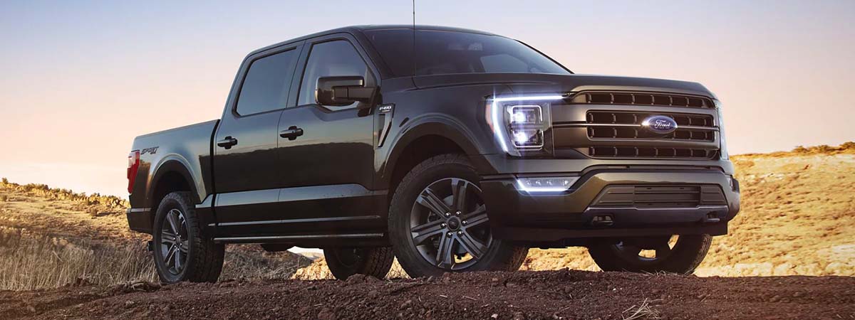 External shot of a 2023 Ford F-150 with the headlights on parked on dirt with a desert in the background.