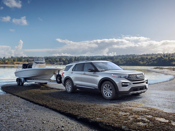 2023 Ford Explorer® Platinum Hybrid in Star White Metallic Tri-coat (extra cost color) towing a boat at a ramp by a lake