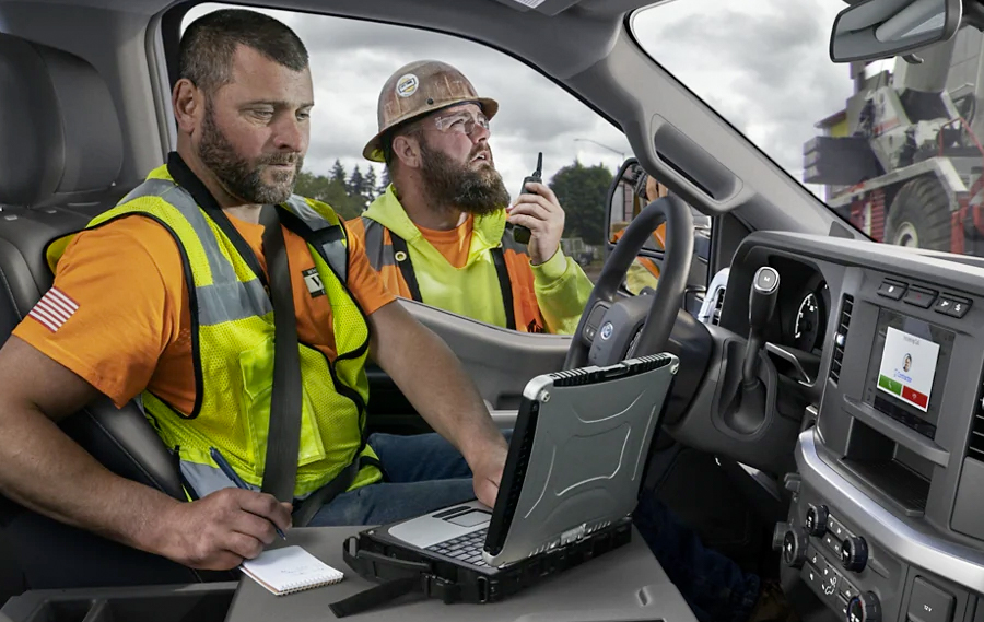 Man working on laptop inside a 2023 Ford Super Duty® F-250® XL with a worker in background