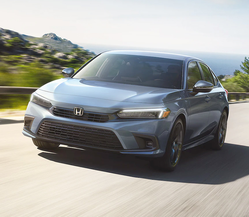 Front driver-side view of the 2023 Honda Civic Sport Sedan in Sonic Gray Pearl, accelerating up a hill.