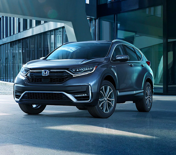 Front driver-side view of the 2022 CR-V Hybrid Touring in Modern Steel Metallic, parked in front of a modern office building.