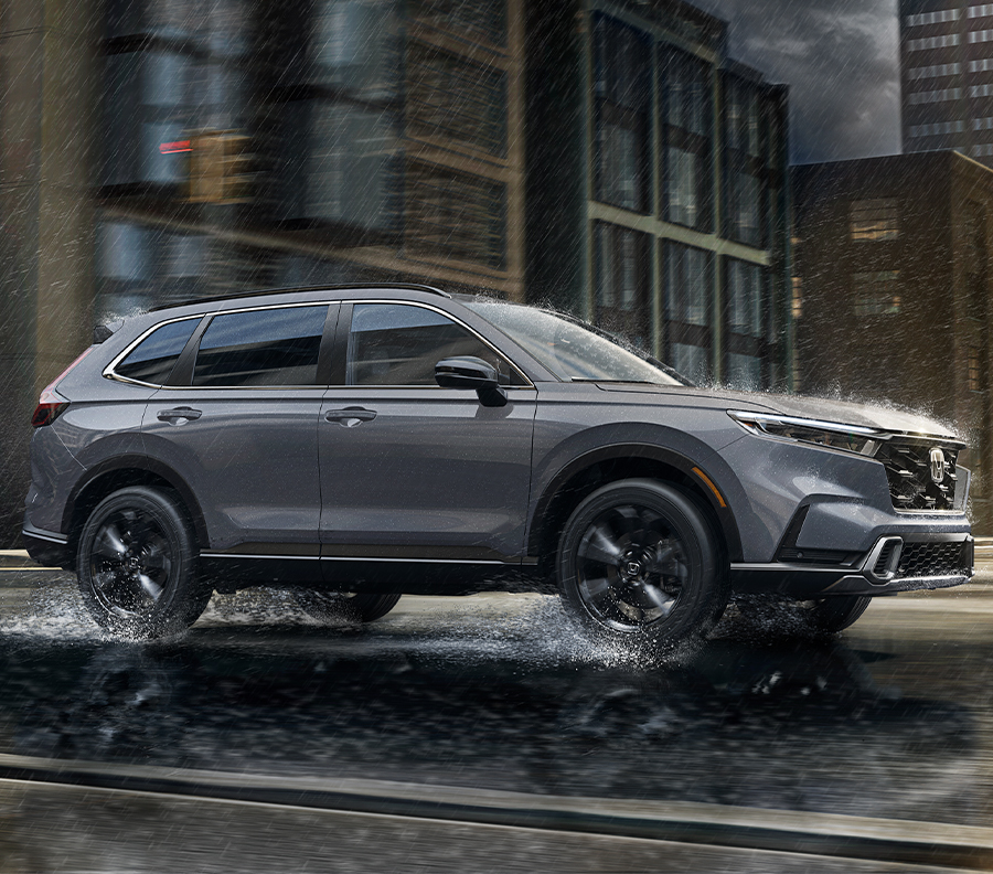 Side shot of silver 2023 Honda CR-V driving on rainy street.