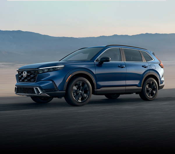 The 2023 Honda CR-V driving along a street with mountains in the background