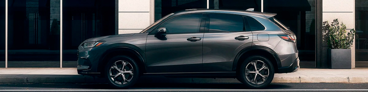 Driver-side view of the 2023 Honda HR-V EX-L in Modern Steel Metallic shown parked next to an office building.