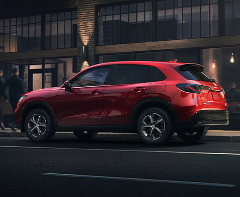 Rear driver-side view of the 2023 Honda HR-V EX-L in Milano Red shown parked next to a modern restaurant.