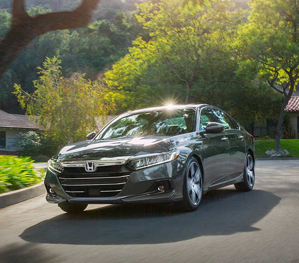 Front driver-side view of the 2022 Honda Accord Hybrid Touring in Modern Steel Metallic, driving through residential neighborhood.