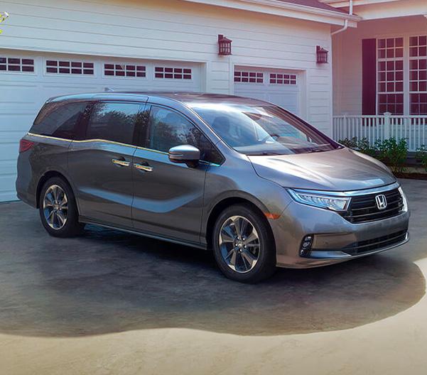 Tackle the first day of school — or any day — with ease and comfort. Front 3/4 shot of 2023 Honda Odyssey in front of garage.