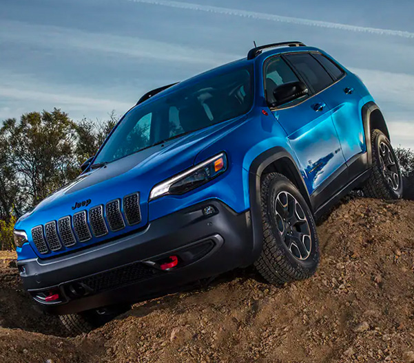 A blue 2023 Jeep Cherokee Trailhawk crawling over a large mound of dirt.