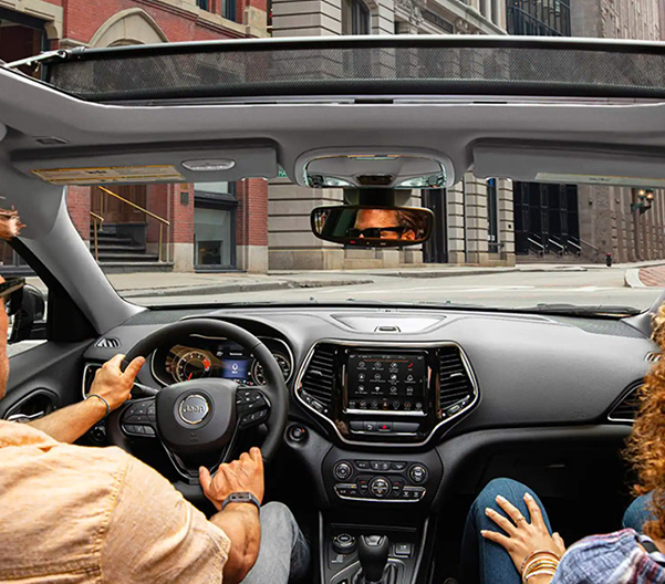 The interior front seat area of the 2023 Jeep Cherokee Altitude Lux with the available Commandview Dual-Pane Panoramic Sunroof open.
