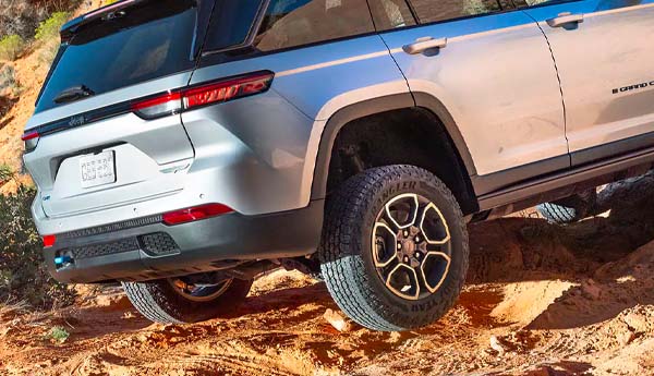 The rear view of a 2023 Jeep Grand Cherokee 4XE driving uphill in a rural road.