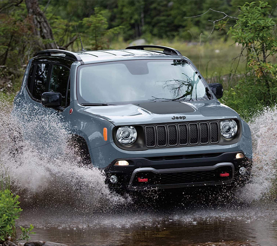 A gray 2023 Jeep Renegade Trailhawk being driven through a stream with water spraying up to the windows.