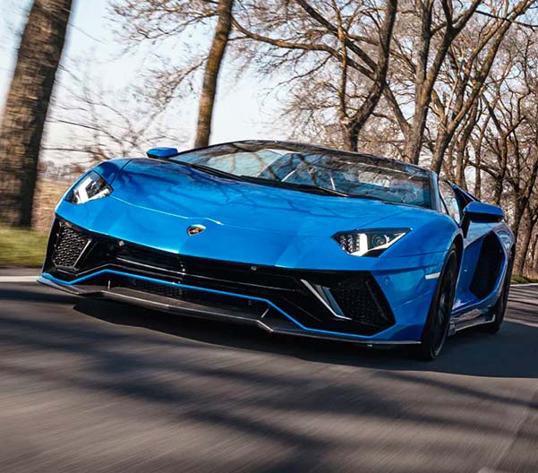 Exterior shot of a 2023 Lamborghini Aventador driving down a road during the daytime.