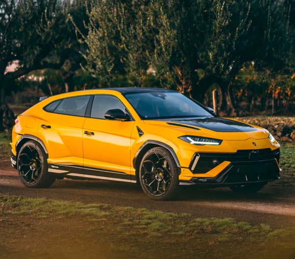 An exterior shot of a yellow Lamborghini Urus driving on a dirt road during the daytime.