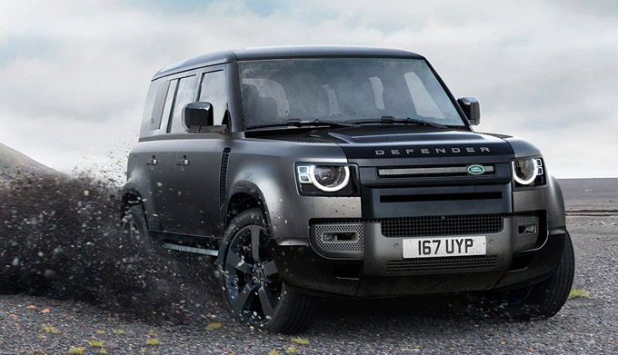 Exterior shot of a 2023 Land Rover Defender driving on gravel.