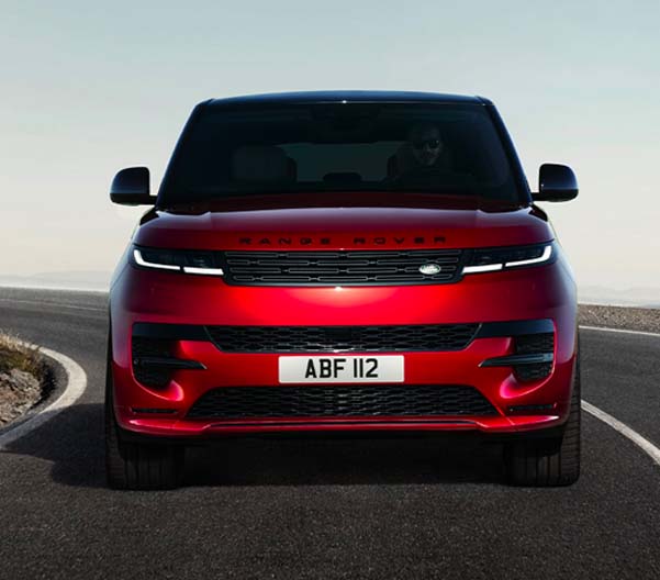 Exterior shot of a red 2023 Range Rover Sport driving on a rural street.