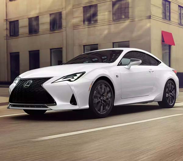 Exterior shot of a white 2023 Lexus RC driving down a city street during the day.