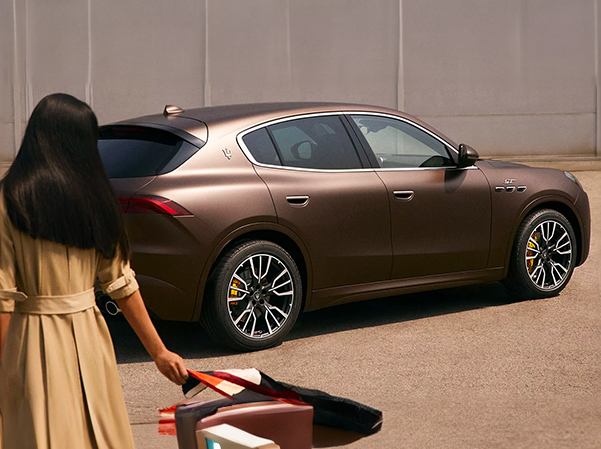 Rear 3/4 shot of 2023 Maserati Grecale with woman walking by it in daytime.