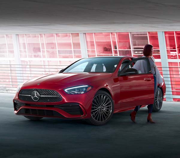 Exterior shot of a person getting out of a red 2023 Mercedes-Benz C-Class in a garage.