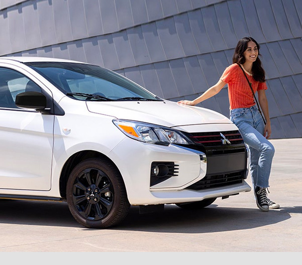 Woman leaning on a parked white 2023 Mitsubishi Mirage hatchback