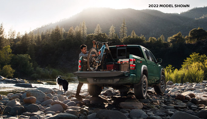 The 2022 Nissan Frontier parked on rocks with a bike being loaded into the truck bed