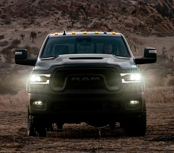 A head-on view of a 2023 RAM 2500 Rebel being driven off-road, in the desert at dusk, with its headlamps on.