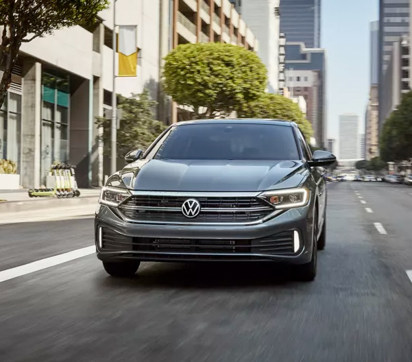 Jetta shown in Platinum Gray Metallic as seen from the front driving on a modern city street.