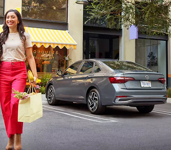 Two people walk away from a Jetta shown in Platinum Gray Metallic parked in front of a flower store.