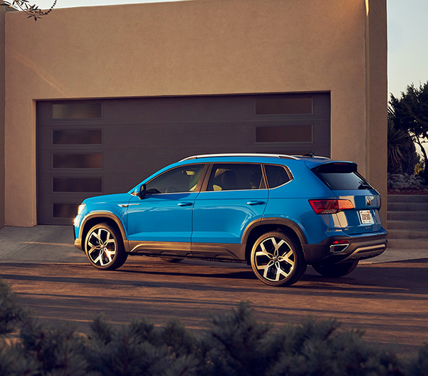 A Taos in Cornflower Blue is seen from its drivers side, parked in the driveway of a desert home.