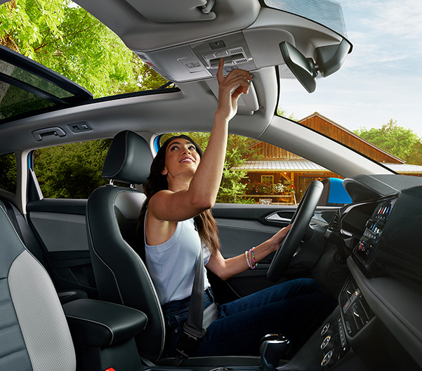 Woman in the driver’s seat of a Taos presses an overhead button to open the available panoramic sunroof.