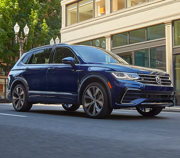 A Tiguan shown in Atlantic Blue Metallic drives through a modern, downtown area.