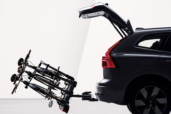 An open tailgate and a bicycle holder attached by tow bar folded down on the rear of a Volvo XC60 Recharge.