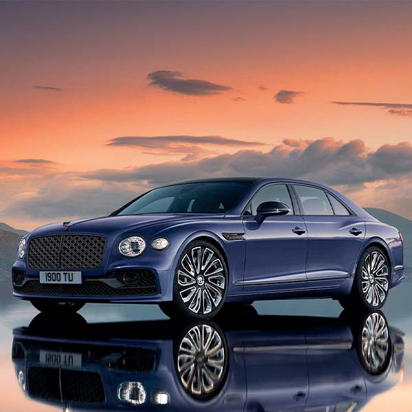The 2024 Bentley Flying Spur parked on a reflective surface with a sunset in the background