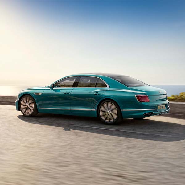 Side view of the 2024 Bentley Flying Spur driving along a road in front of the ocean