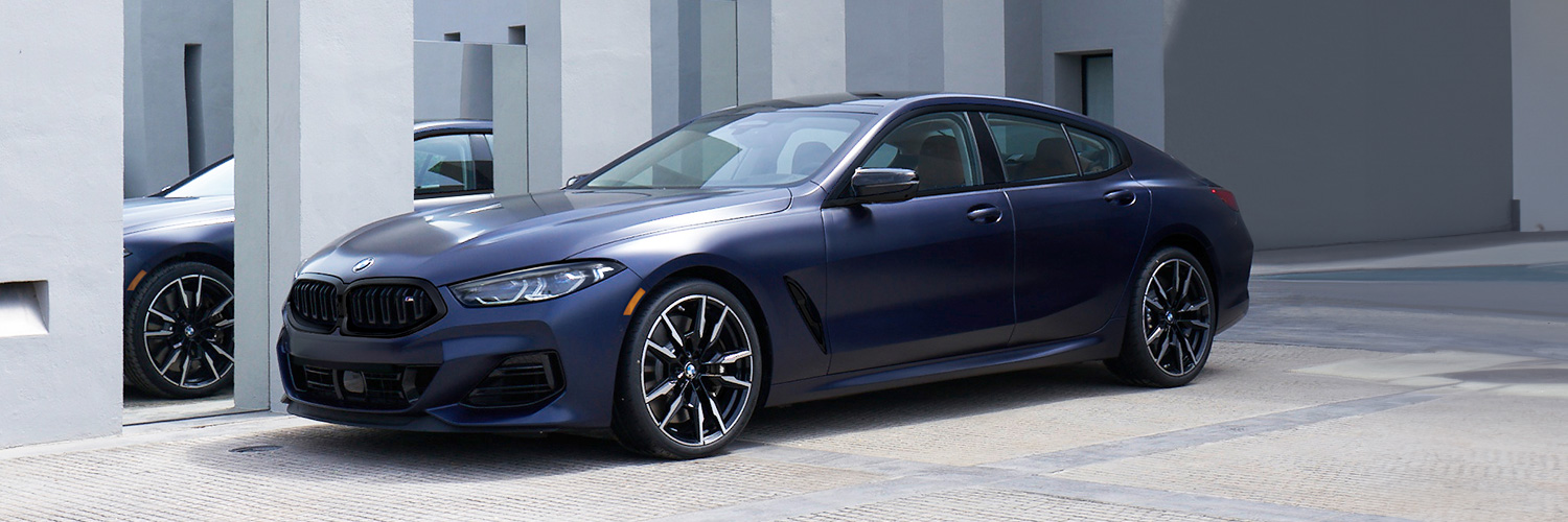 A 2024 BMW 8 SERIES Sedan parked in front of an ultra-modern building