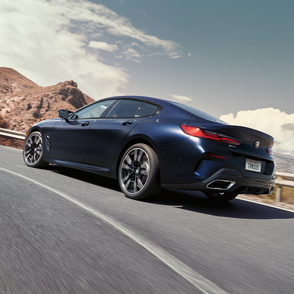 Rear shot of 2024 BMW  -Series driving up winding road.