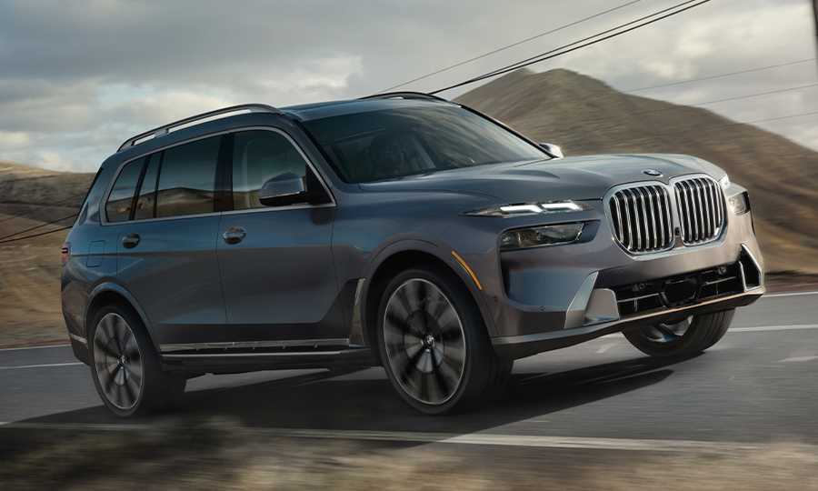 Passenger side view of the 2024 BMW X7 driving down a mountain highway