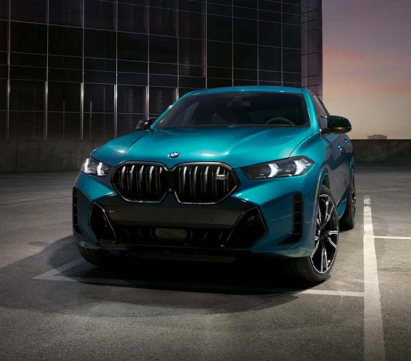 Exterior shot of a 2024 BMW X6 parked in an empty parking lot at night.