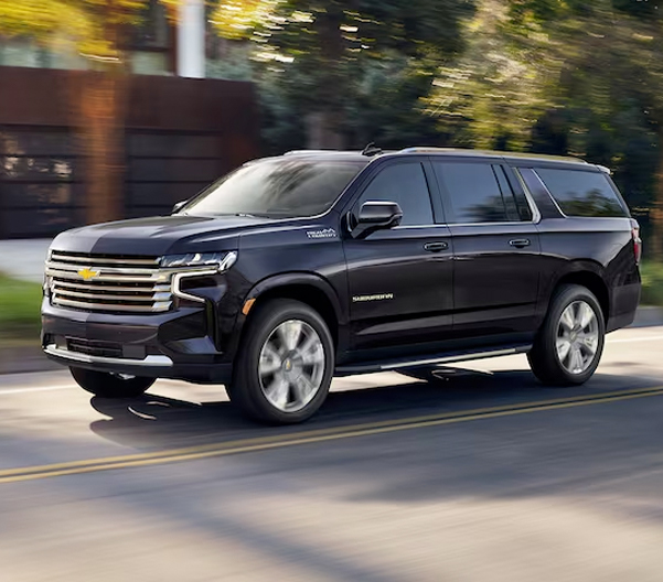 The Dark Ash Metallic MY24 Chevy Suburban Cruising Through a Residential Neighborhood
