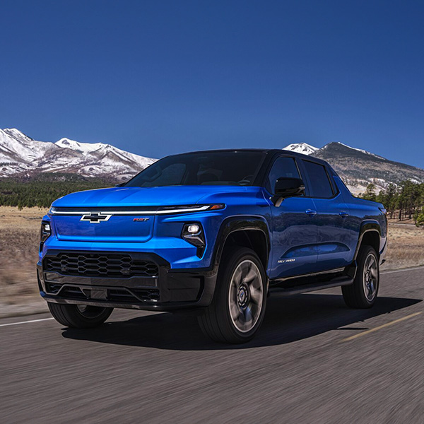 2024 Chevy Silverado EV Driving Down A Road With Mountains In The Background
