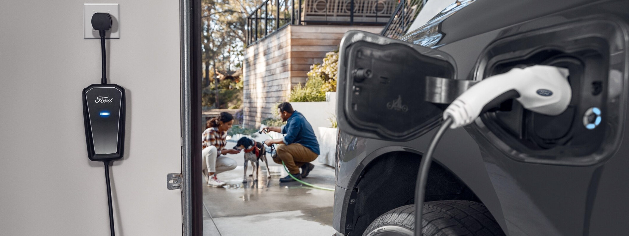 A Ford F-150® Lightning being charged inside a garage next to two people washing a dog