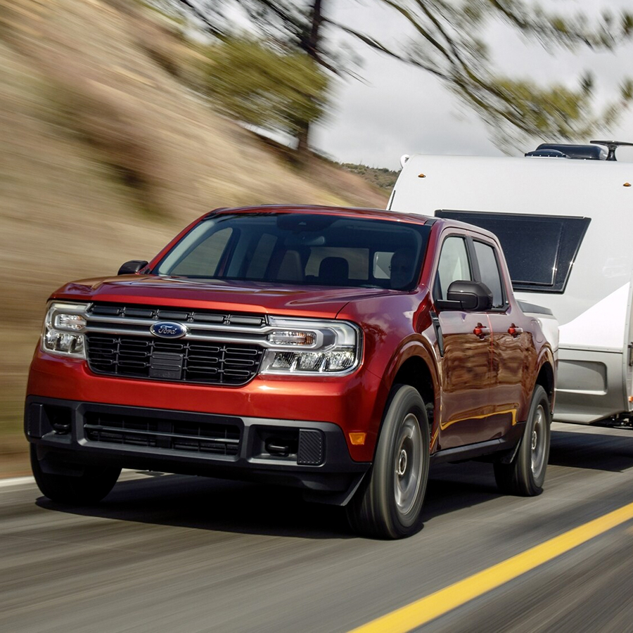 A 2024 Ford Maverick® truck in Hot Pepper Red is being driven on a road in a scenic location.